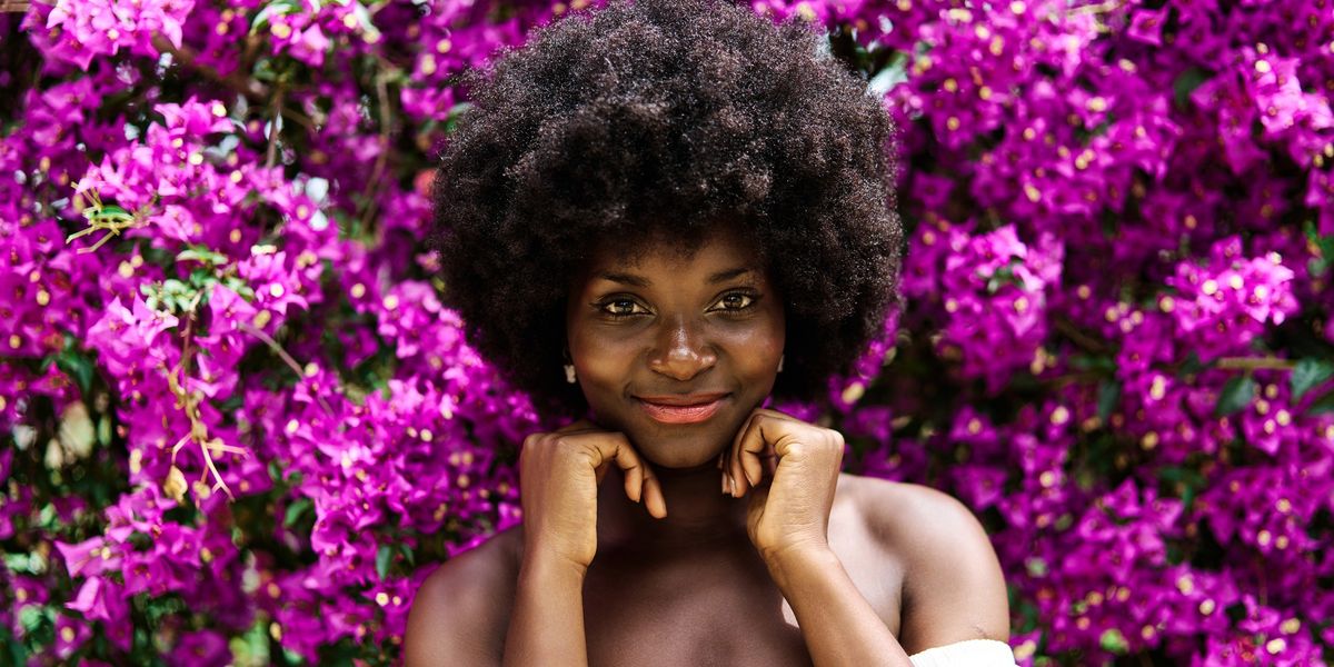 Beautiful-Black-woman-with-afro-smiling-in-front-of-a-wall-of-purple-flowers