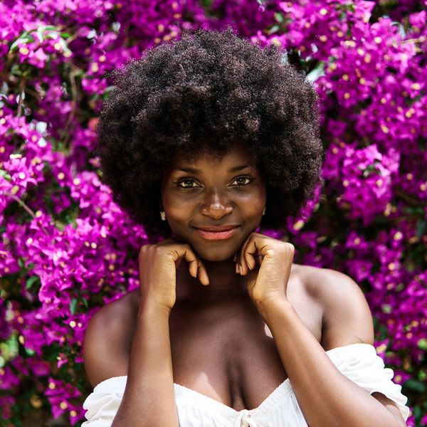 Beautiful-Black-woman-with-afro-smiling-in-front-of-a-wall-of-purple-flowers