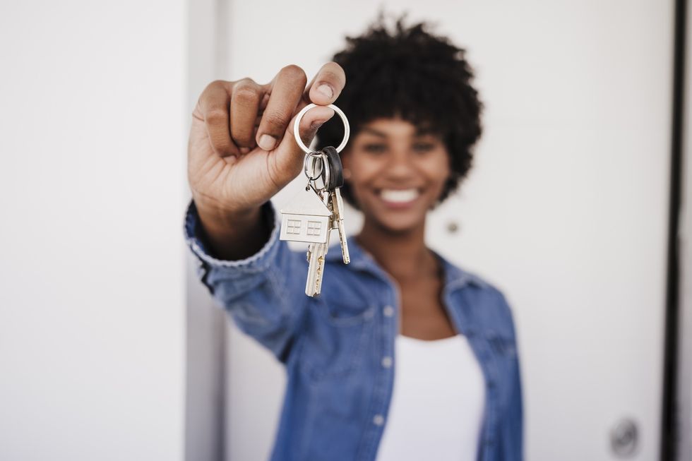 Happy-woman-showing-house-keys-standing-in-front-of-door