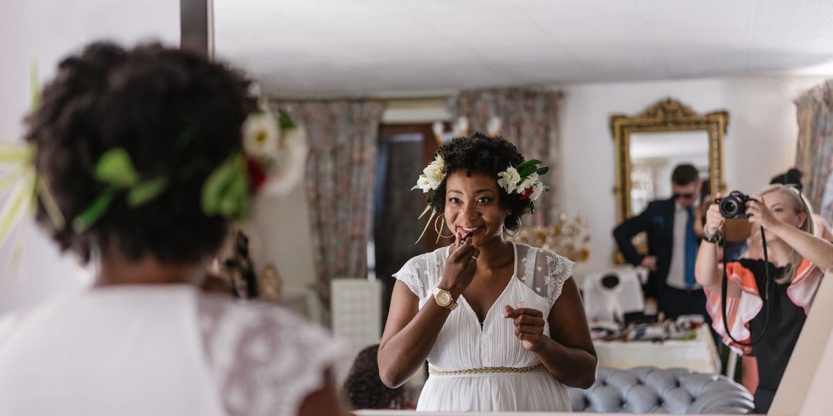 Bride-applying-lipstick-in-the-mirror-while-being-photographed-on-her-wedding-day