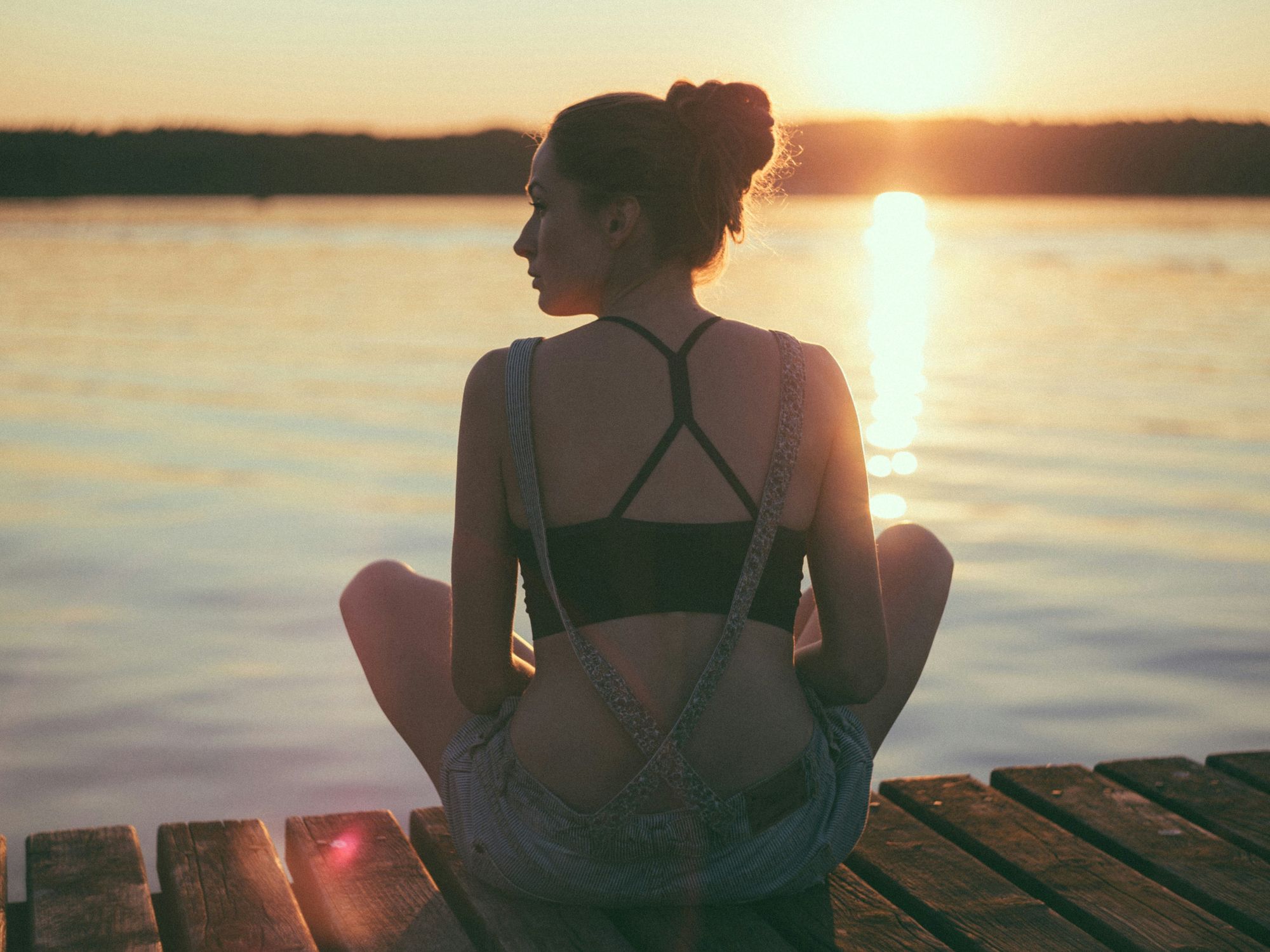 woman sitting on brown wooden dock during sunset