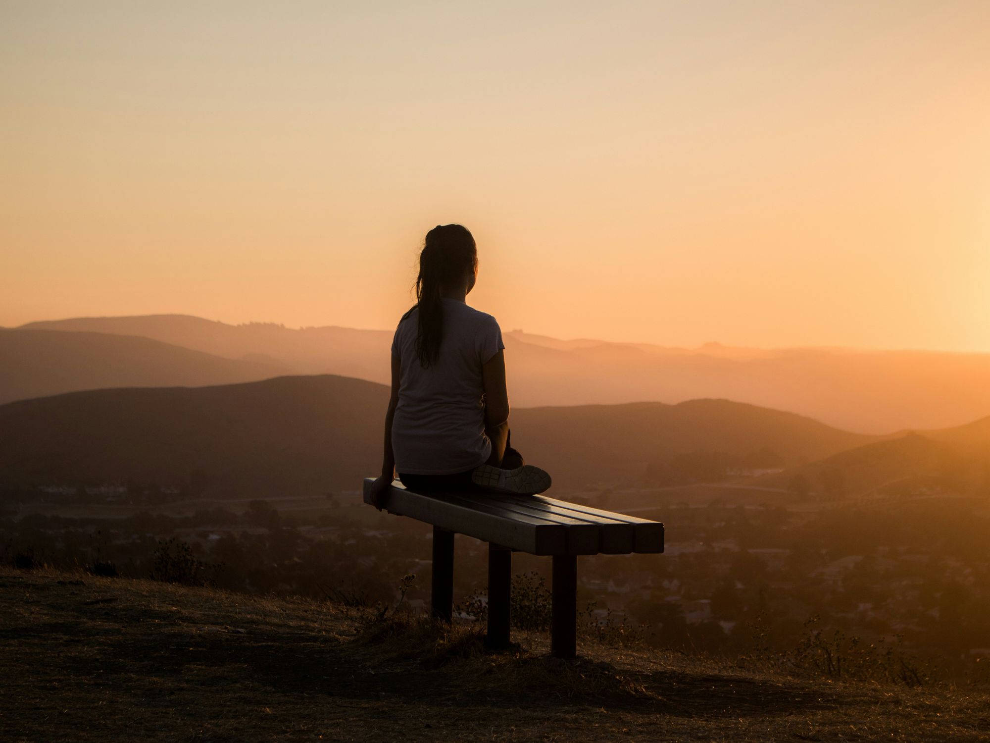 woman sitting on bench over viewing mountain at sunset