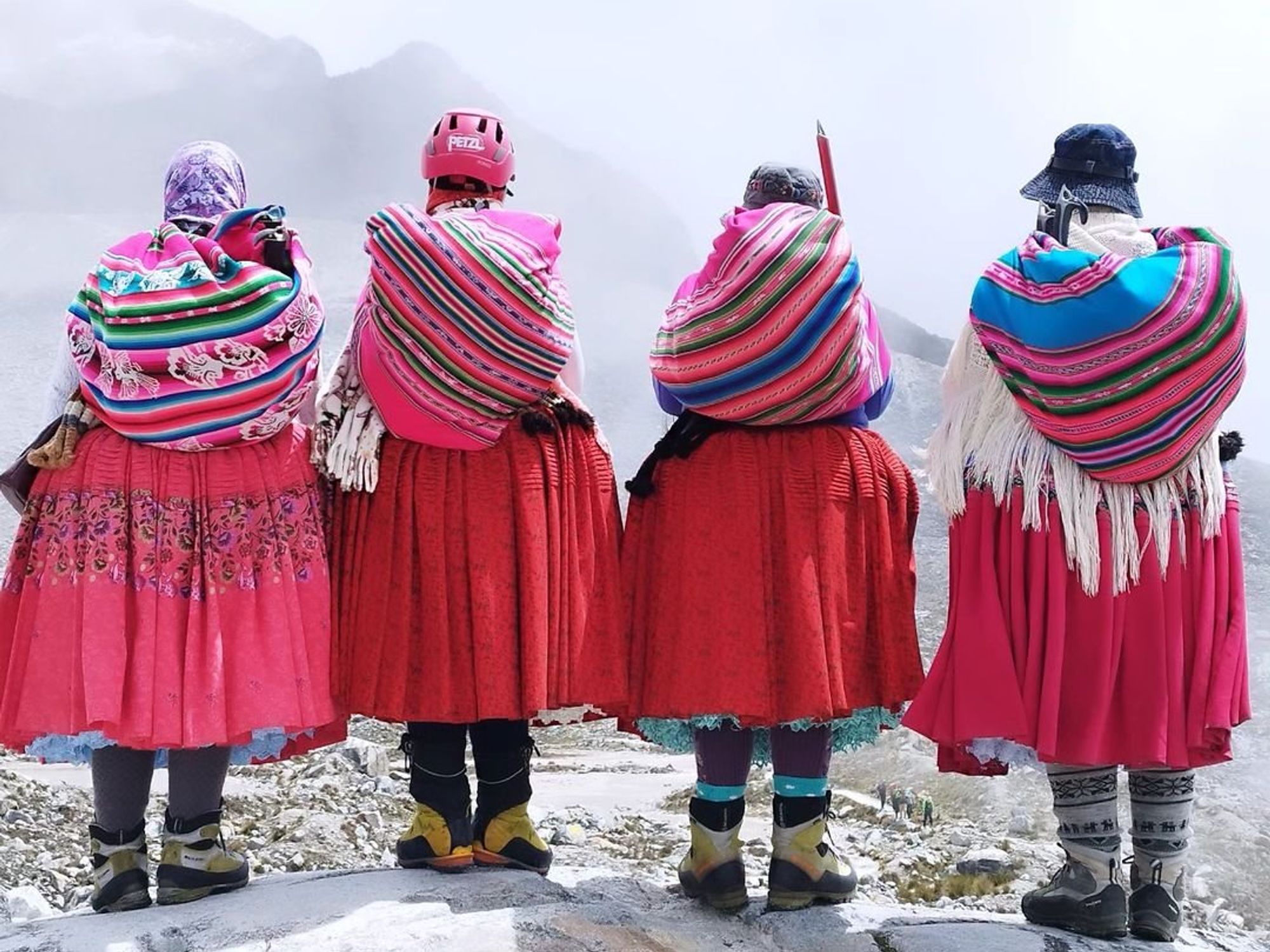 Four Bolivian cholitas, in traditional attire, admiring the mountain landscape during their climbing expedition.