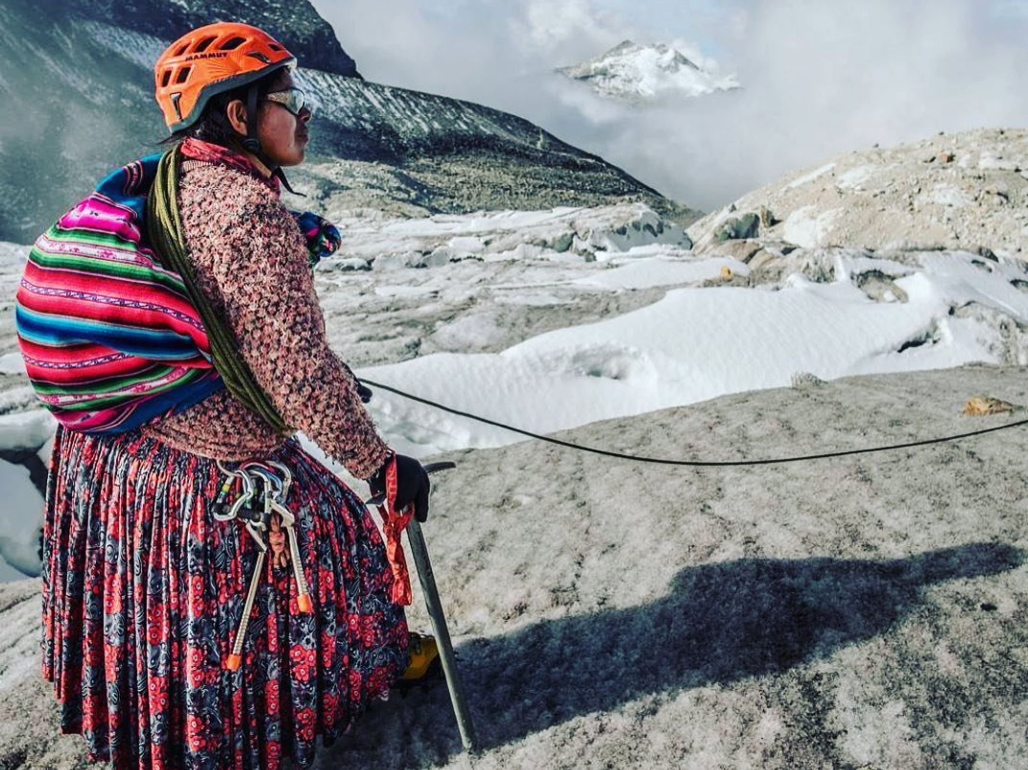 A Bolivian cholita, in traditional attire, admiring the mountain landscape during a climbing expedition.