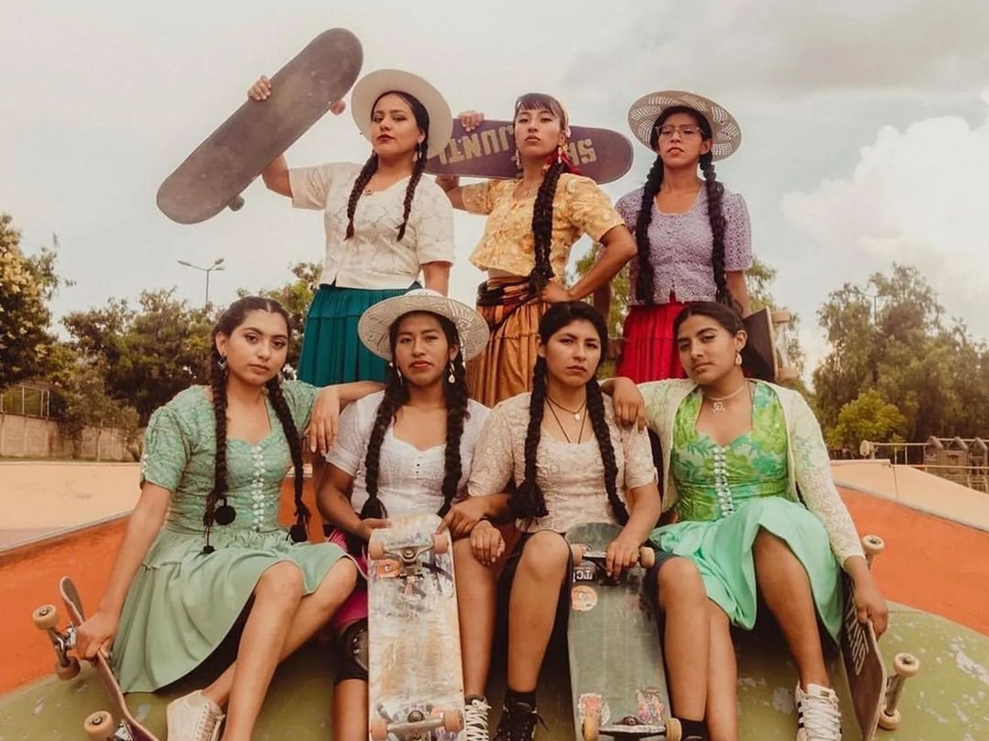 Bolivian cholitas, dressed in their traditional attire holding skateboards, showcasing their identity as skilled young female skaters.