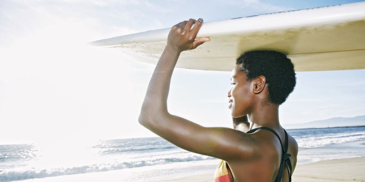 Black-woman-balancing-surfboad-on-her-head-at-the-beach