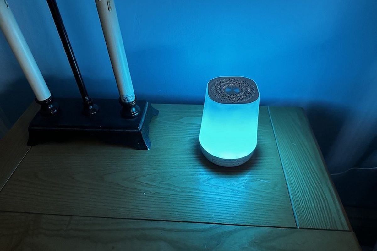 a photo of Momcozy Smart Baby Sound Machine on a nightstand with rainbow colors showing