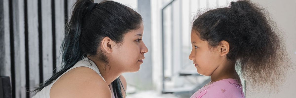 A Latina woman and a Latina girl, both at the same height level, gaze into each other’s eyes.