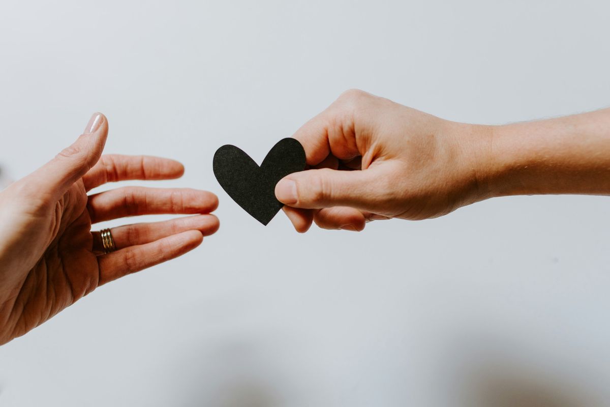 one hand passing a heart to another hand