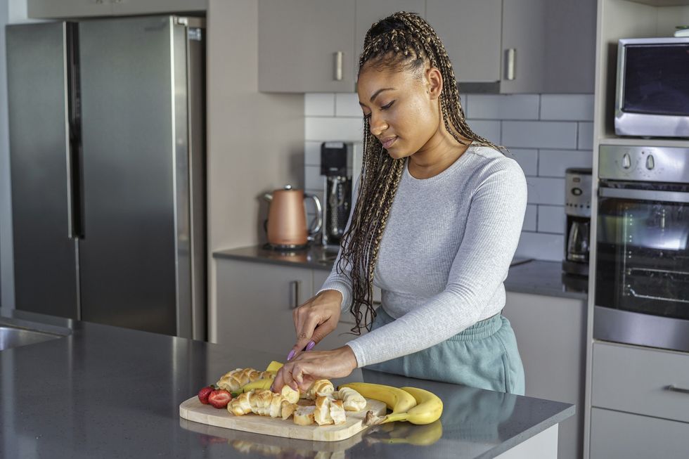 Beautiful-Black-woman-cutting-fruit-on-cutting-board-in-her-kitchen