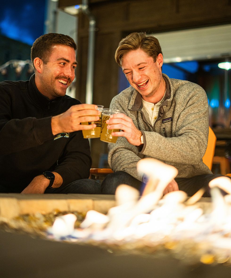 two men making a toast with drinks in front of a fire pit