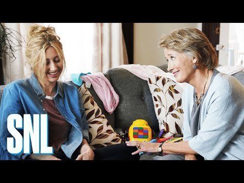 Heidi Gardner and Emma Thompson sitting together on a sofa strewn with toys and clothes