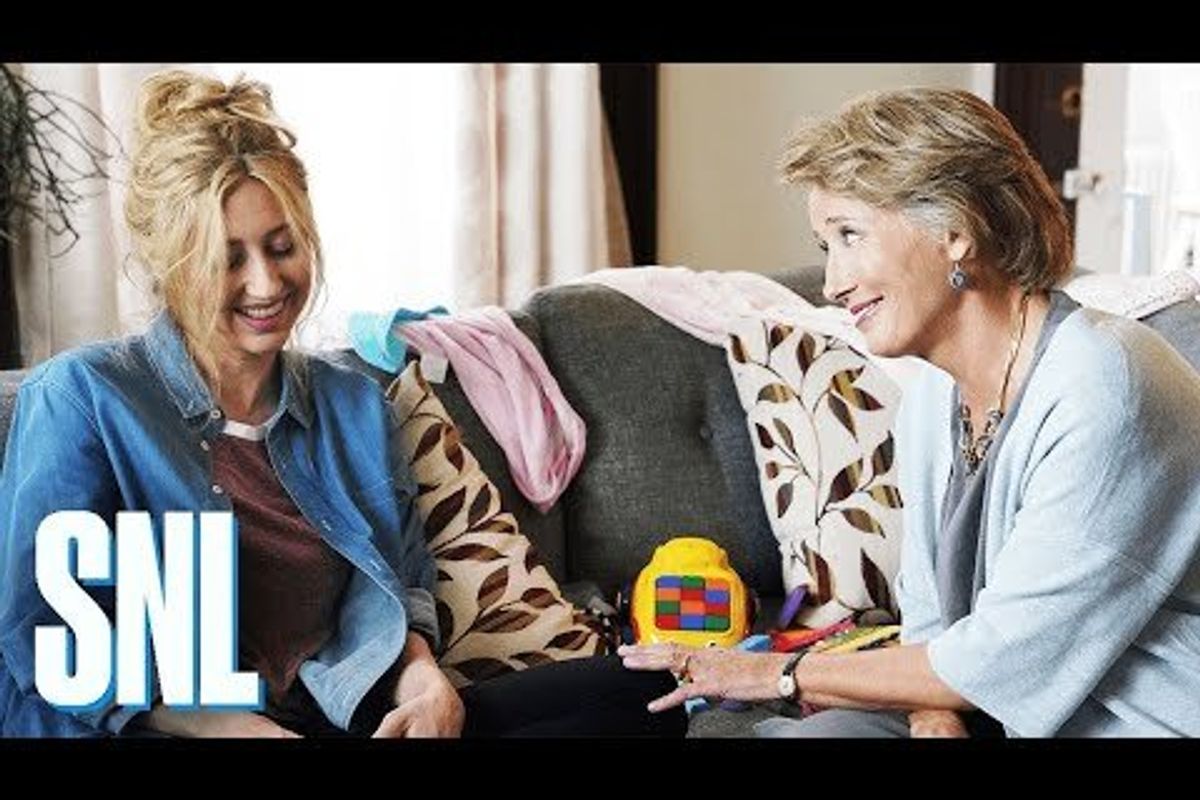 Heidi Gardner and Emma Thompson sitting together on a sofa strewn with toys and clothes