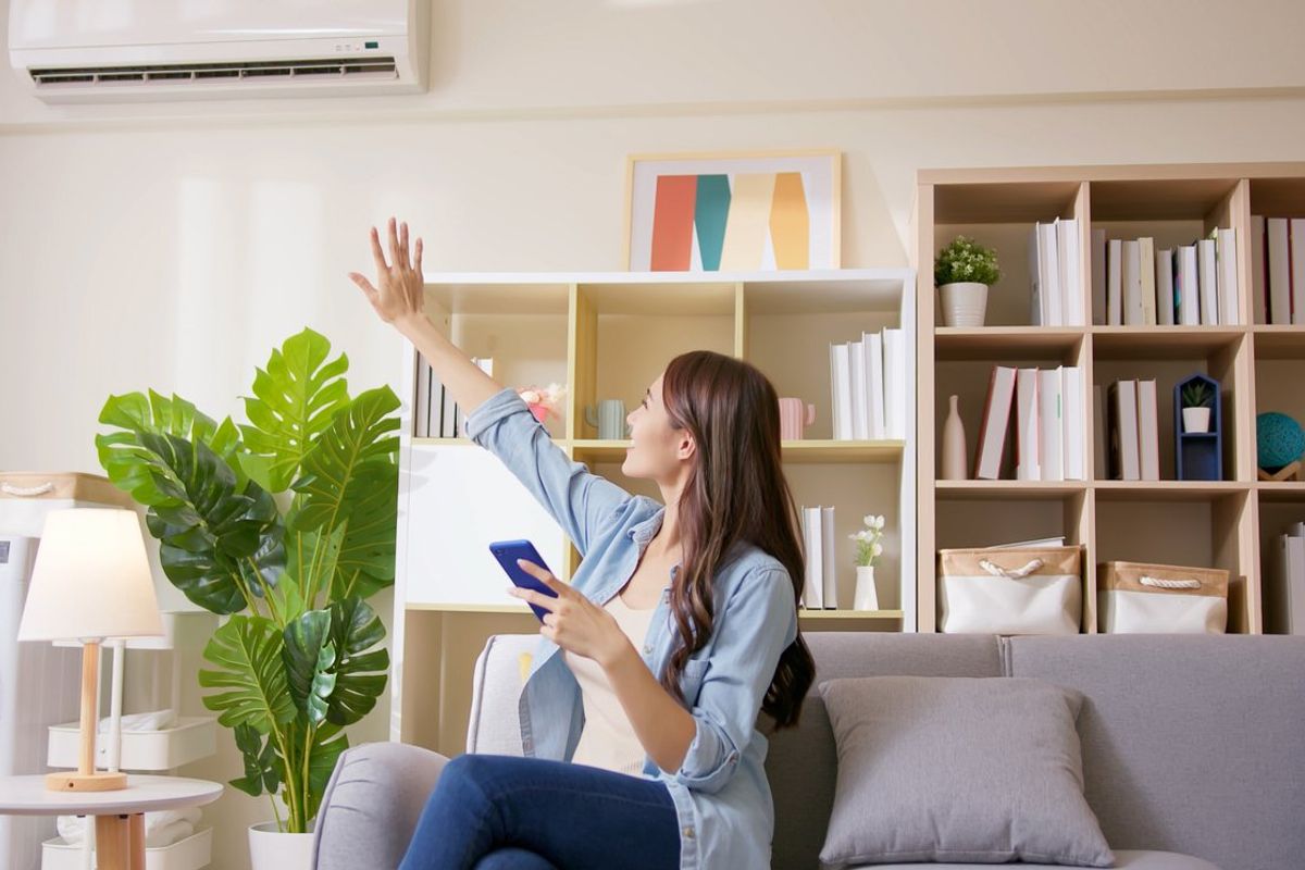 a woman in a room with her smartphone controlling her smart AC unit.