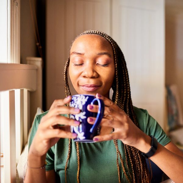 Smiling-Black-woman-with-closed-eyes-deep-breathing-as-she-sips-her-tea-in-bed