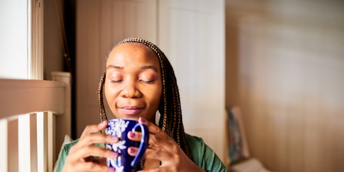 Smiling-Black-woman-with-closed-eyes-deep-breathing-as-she-sips-her-tea-in-bed