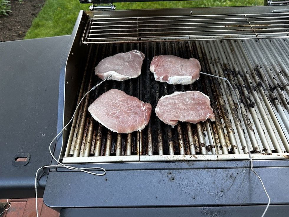 a photo of pork being cooked with wired smart meat thermometers.
