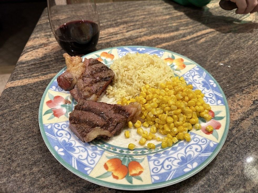 a photo of a plate with steak, corn and rice cooked on an electric grill with a glass of wine.