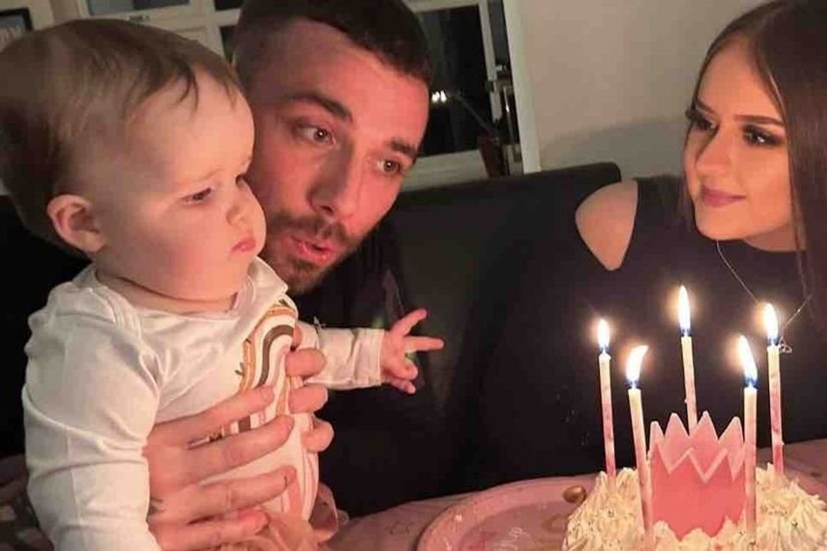 mom and dad holding baby in front of a birthday cake