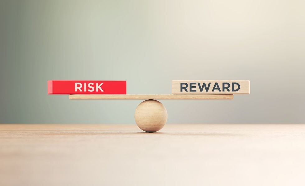a wooden plank on a ball with risk on one end and reward on the other end of the plank balancing