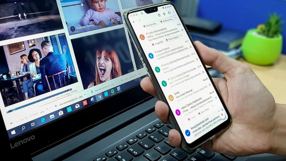 A person using a smartphone and laptop with various open tabs.
