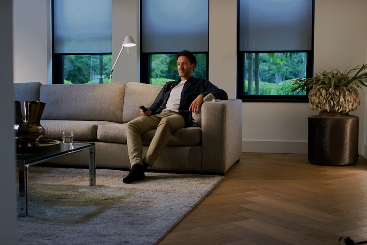 a photo of a man sitting on a couch in a room with Eve MotionBlinds on the windows