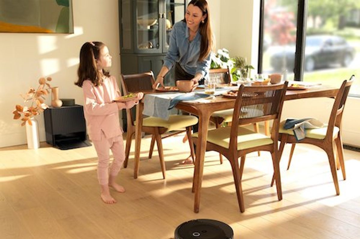 a photo of a woman and child in the dinning room with iRobot's Roomba Combo 10 Max Robot + AutoWash Dock vacuuming the floor