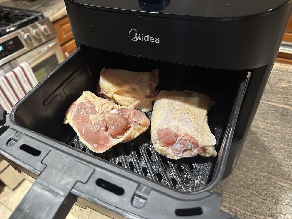 a photo of chicken thighs in the upper basket of Midea Two-Zone Air Fryer basket