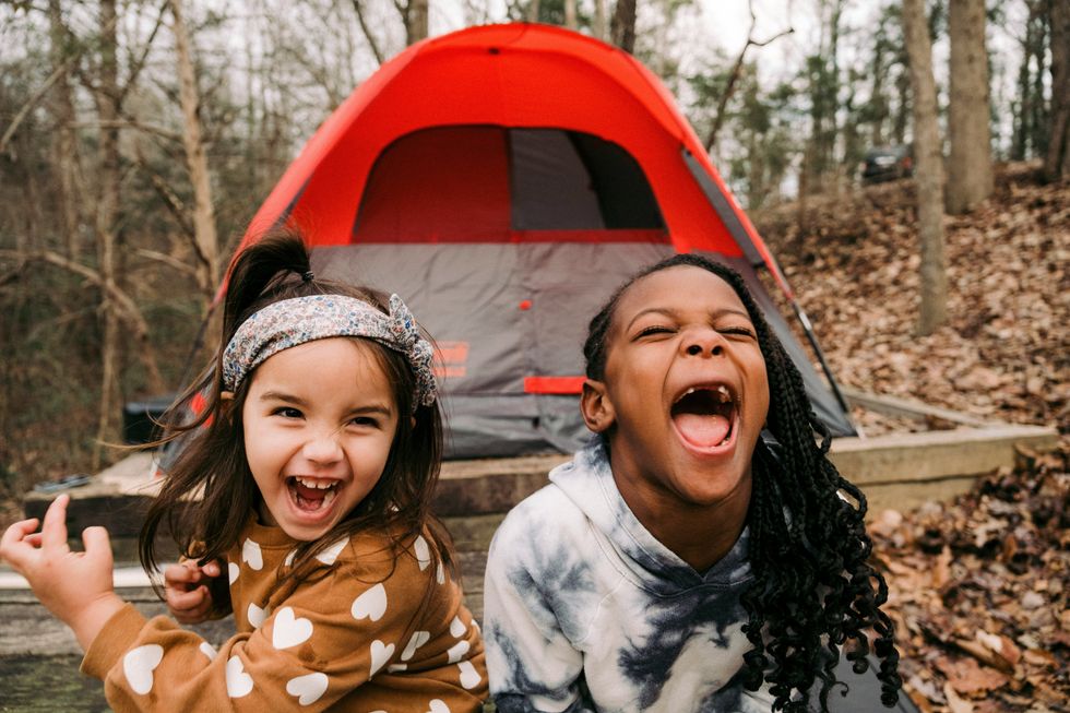two girls stand in front of a camping tent