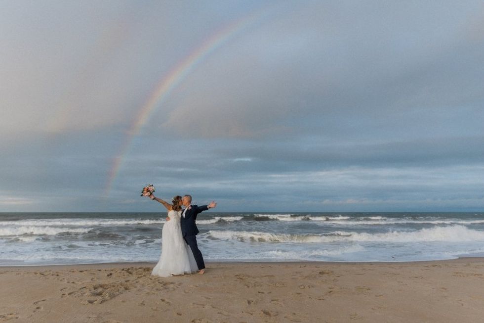 bride and groom on beach in front of rainbow