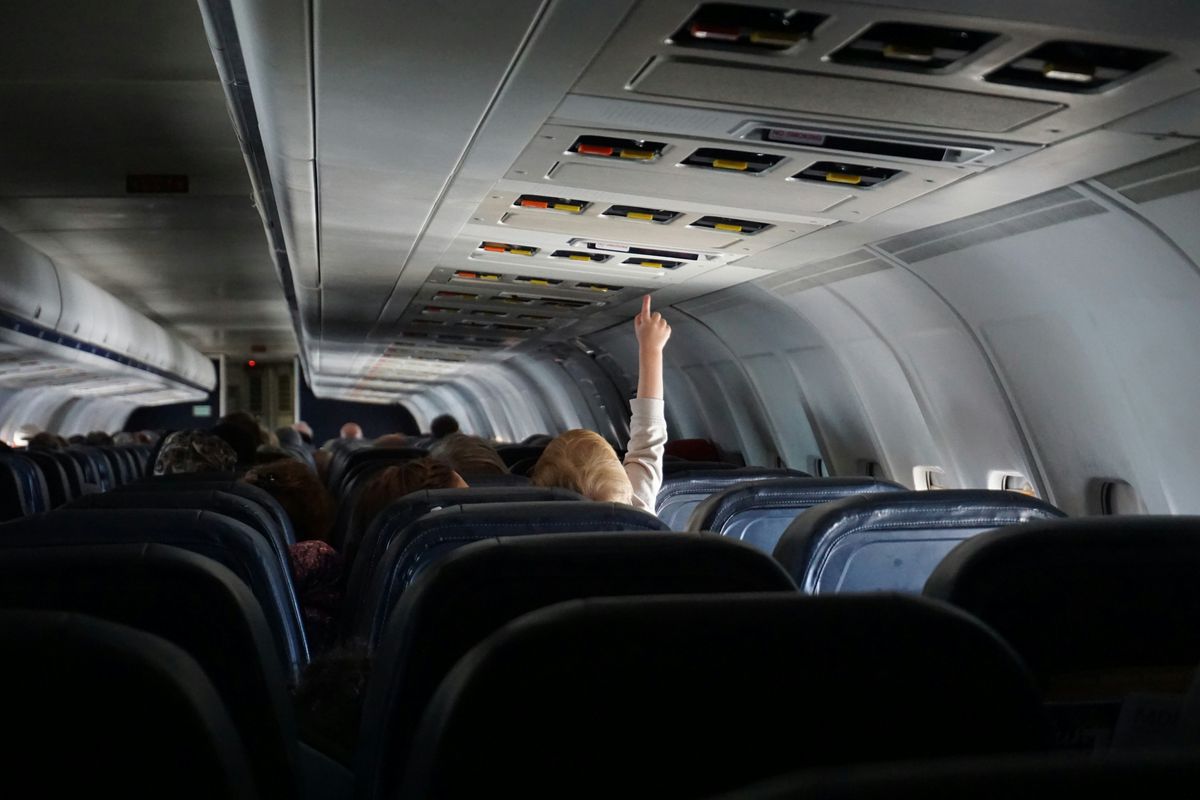 A child on an airplane raising hand to touch attendant button