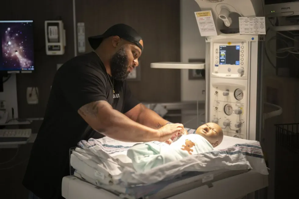 A man practices doula techniques on a baby doll