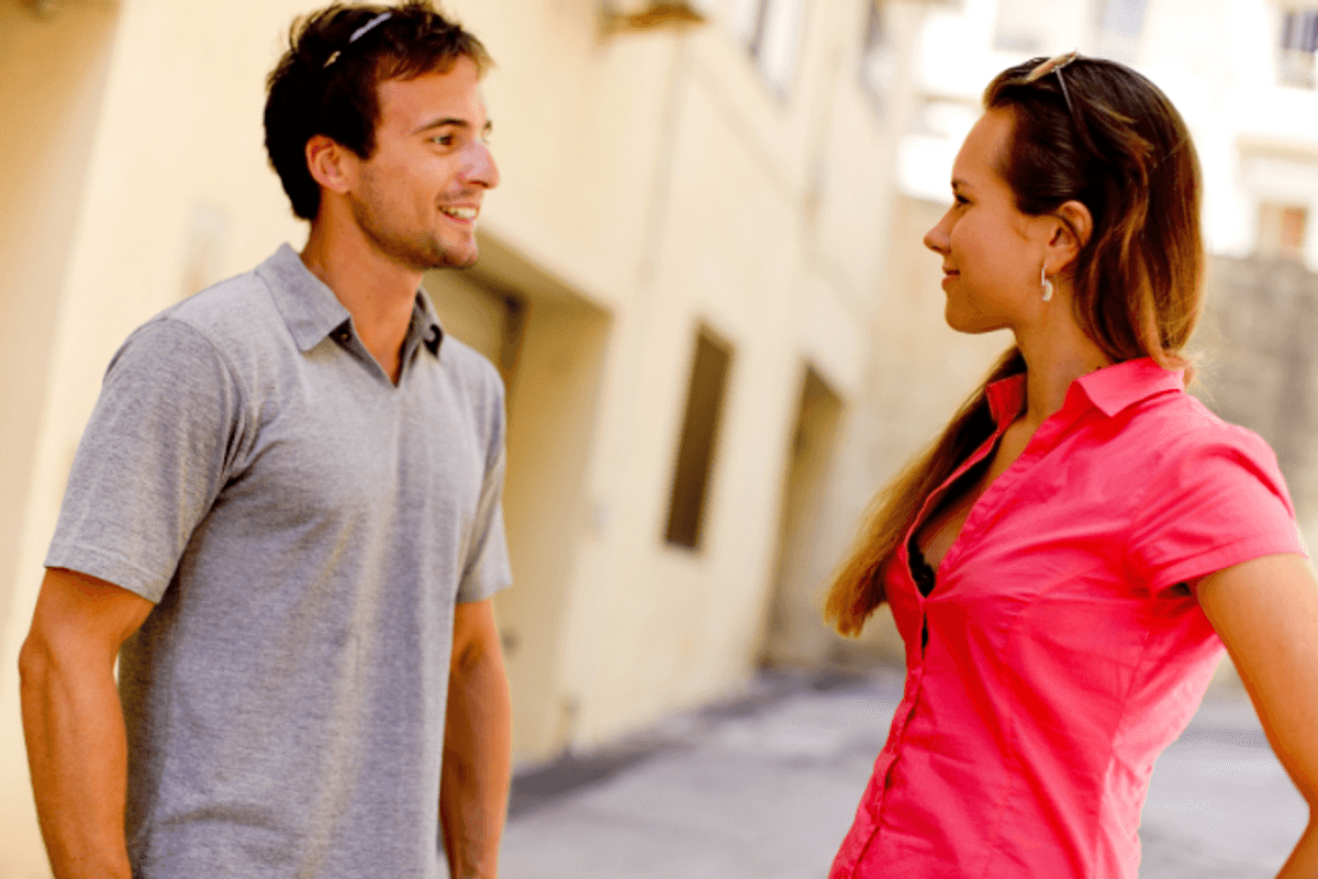 A man in a gray shirt talks to a woman in a pink blouse.