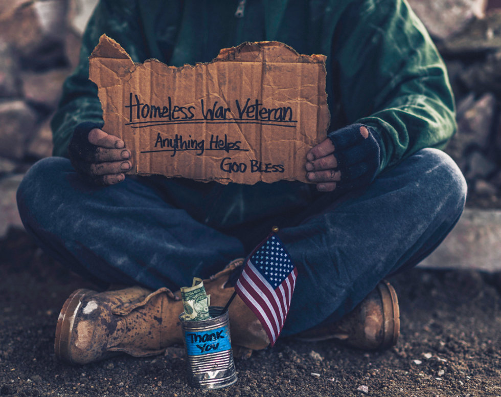 An unhoused veteran sitting with a sign asking for change