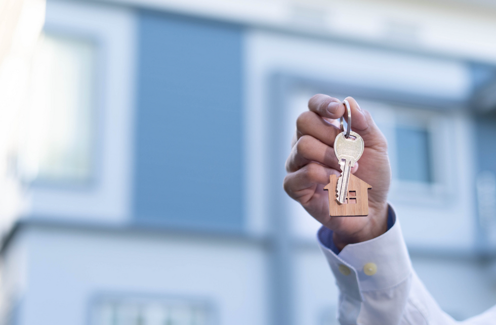 A hand holding house keys in front of a home