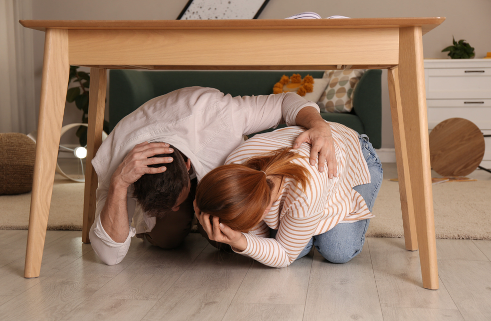 A man and a woman taking shelter under a wooden table