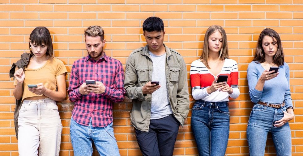 five young adults standing looking at their phones