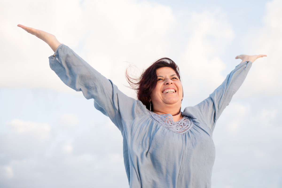 A larger woman with her arms out and smiling outside
