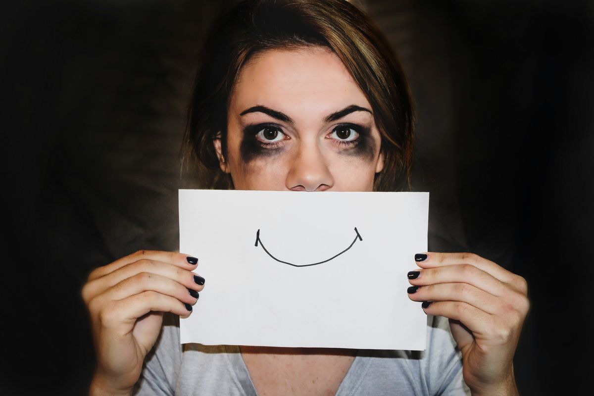 woman with smudged eye makeup holds a sign of a smile over her mouth to look like she's smiling
