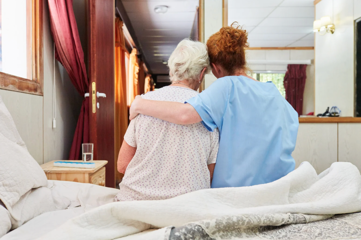 a nurse with her arm around an elderly patient as they sit in bed
