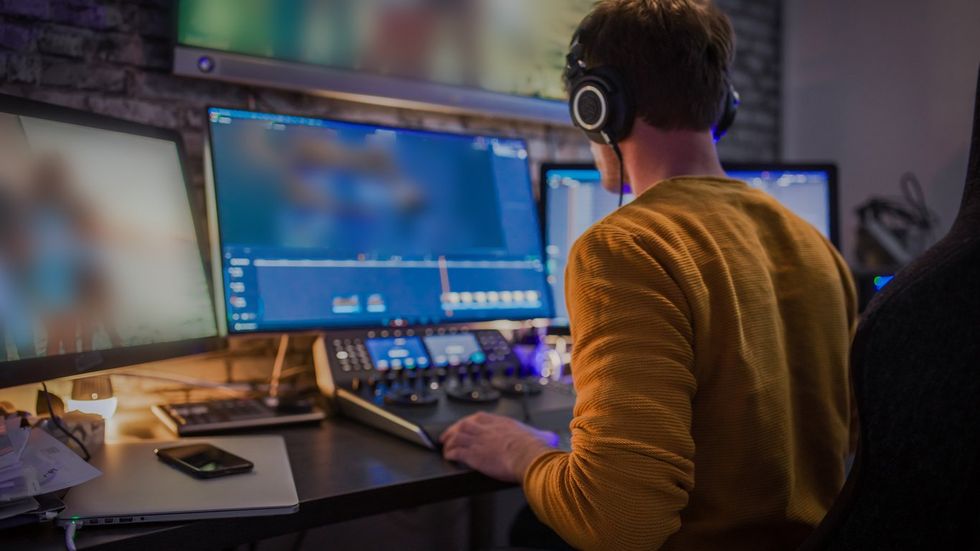 Male editor working with footage on computer screens at desk stock photo