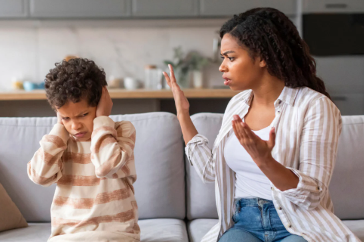 A child covers his ears while his mother looks at him in frustration