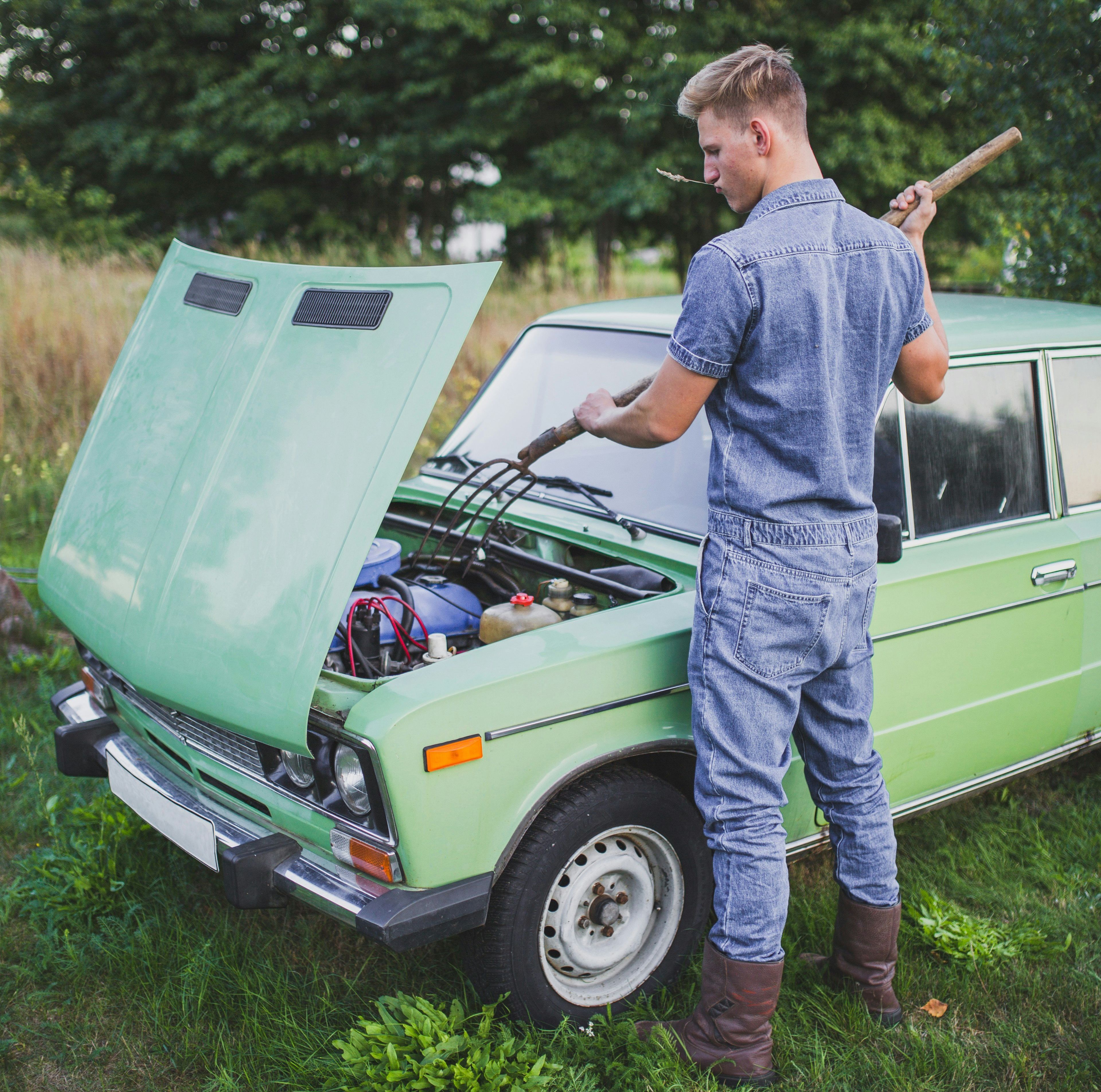 A man stands over an open hood of a green car