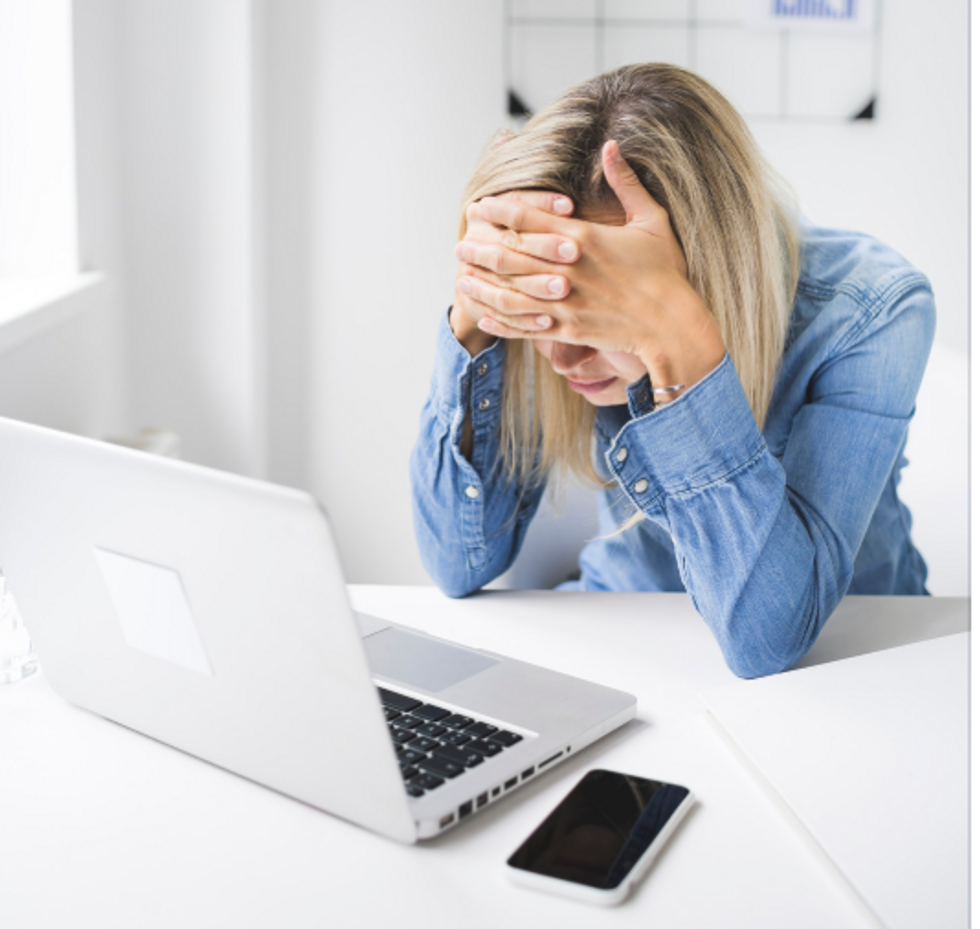 A frustrated woman looks at her laptop with her hands covering her eyes