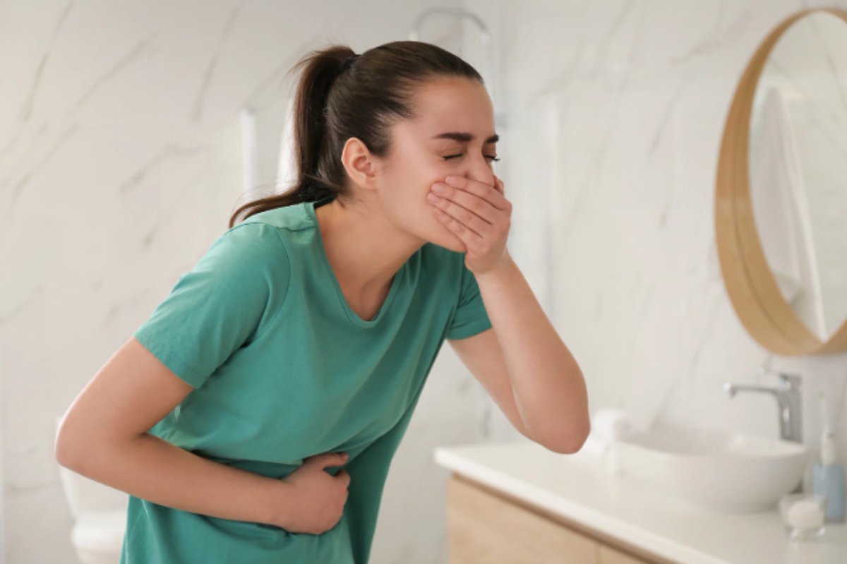 a woman with one hand over mouth and the other over her stomach in a bathroom