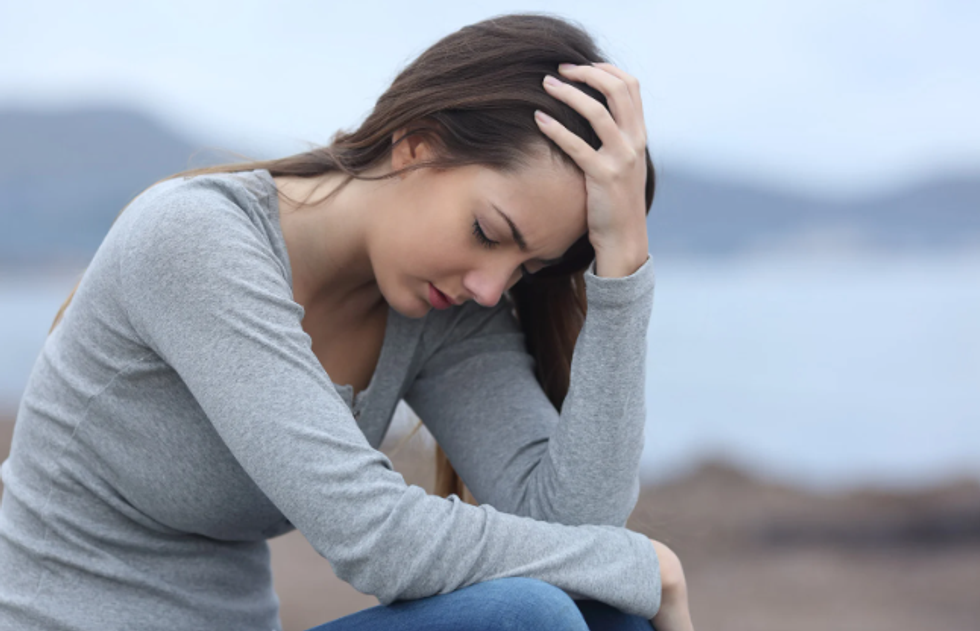 A young women sitting on a blurred beach with her head in one hand