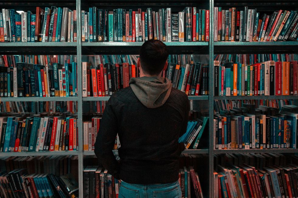 person wearing black and gray jacket in front of bookshelf