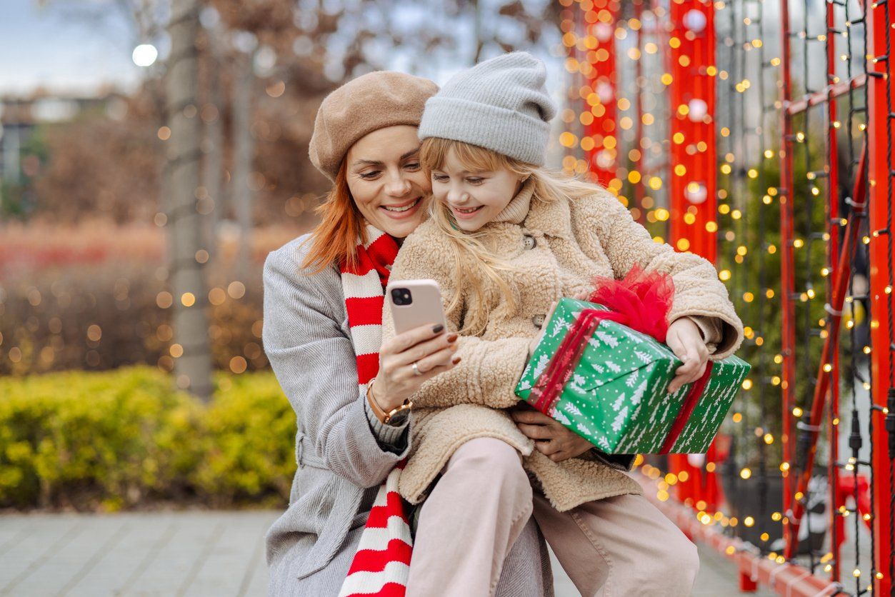 Smiling mother and her cute daughter using smartphone outdoors during Christmas holidays stock photo