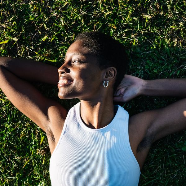 Young black woman relaxing lying on green grass smiling with hands behind head