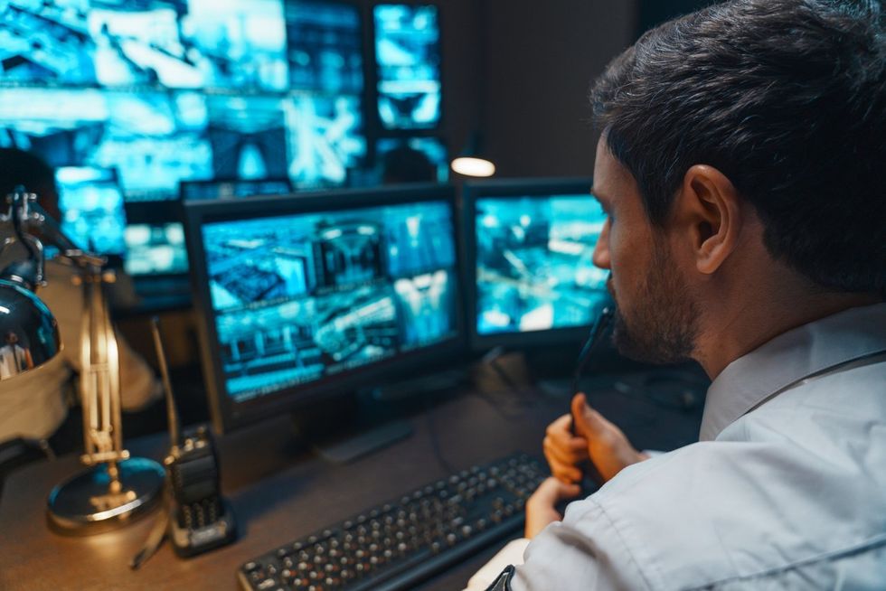 Security Controller with Headset Talk on a Call in security office. Office Room is Full of Desktop Computer Displays with Navigation Screens, Data for the Team. stock photo